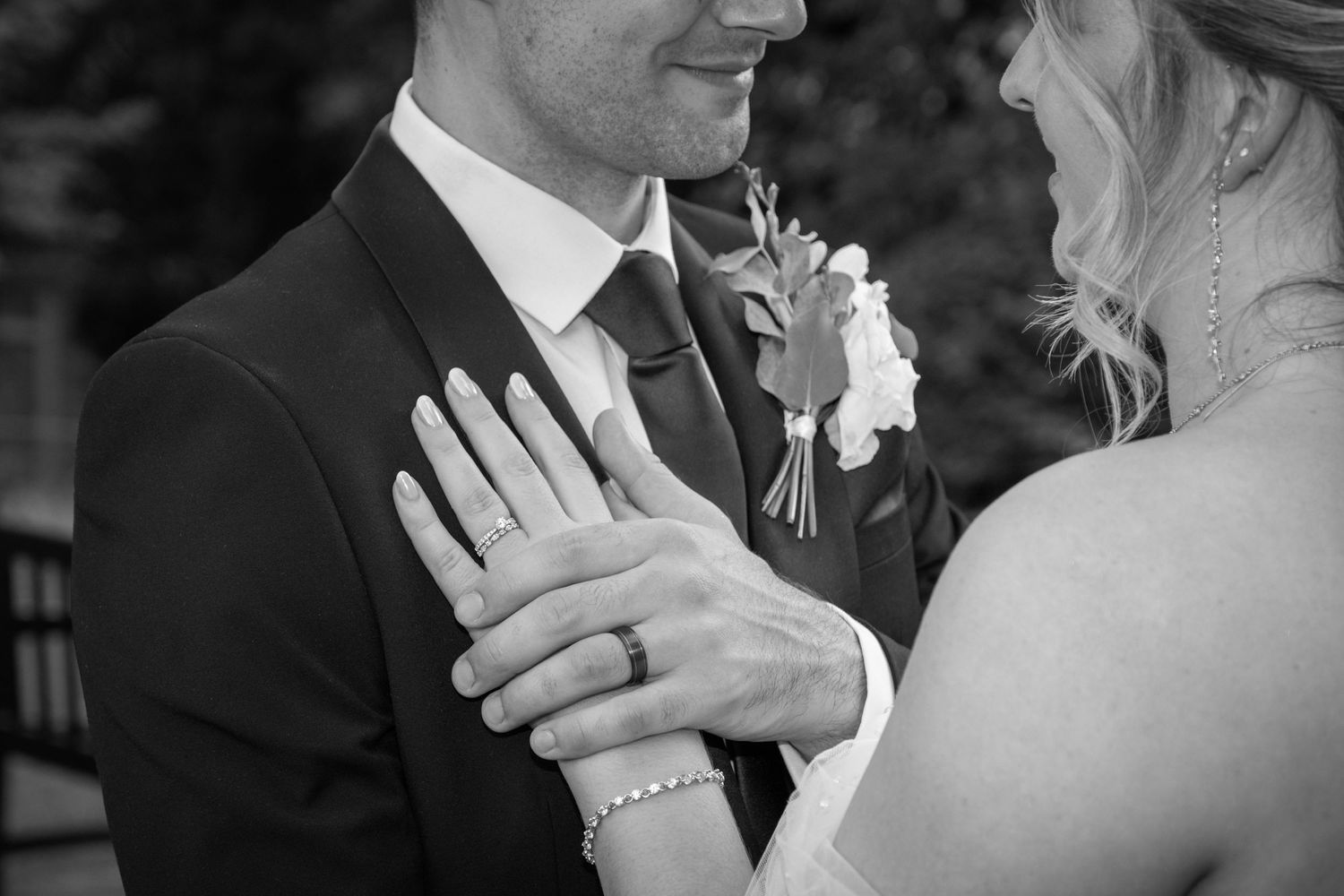 Black and white close-up of wedding rings and hands with delicate bracelet details.
