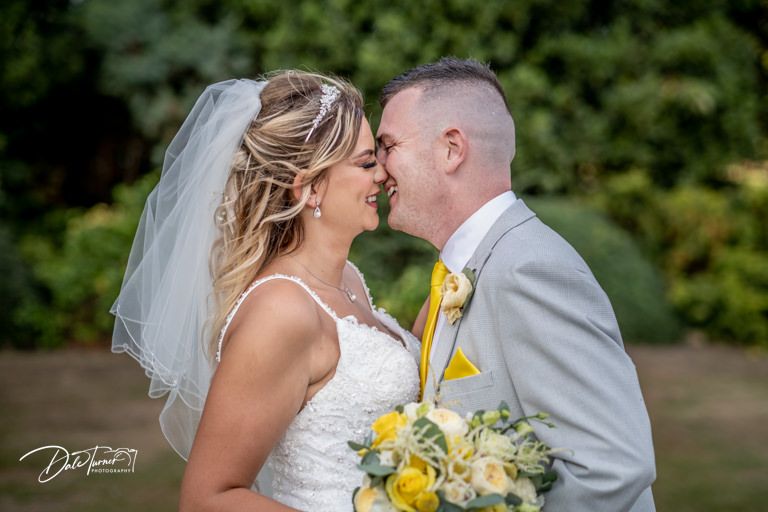 Intimate wedding moment captured in a lush outdoor setting with yellow bouquet accents.