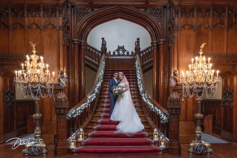 Elegant grand hall with ornate wooden details, red carpet, and crystal chandeliers.