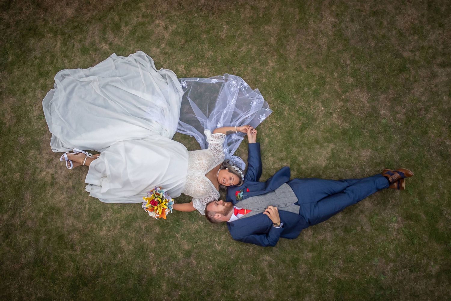 Creative wedding photography with couple laying on grass in formal attire.