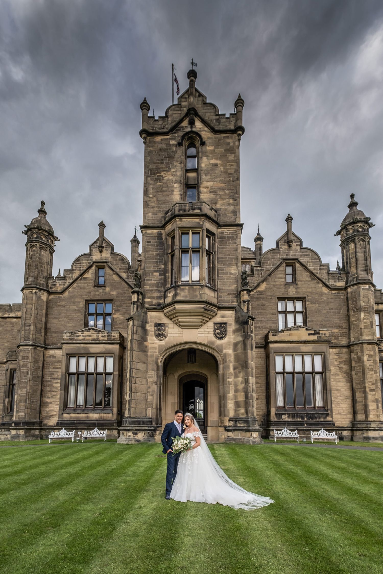 Gothic stone castle wedding venue with manicured lawn under moody sky.