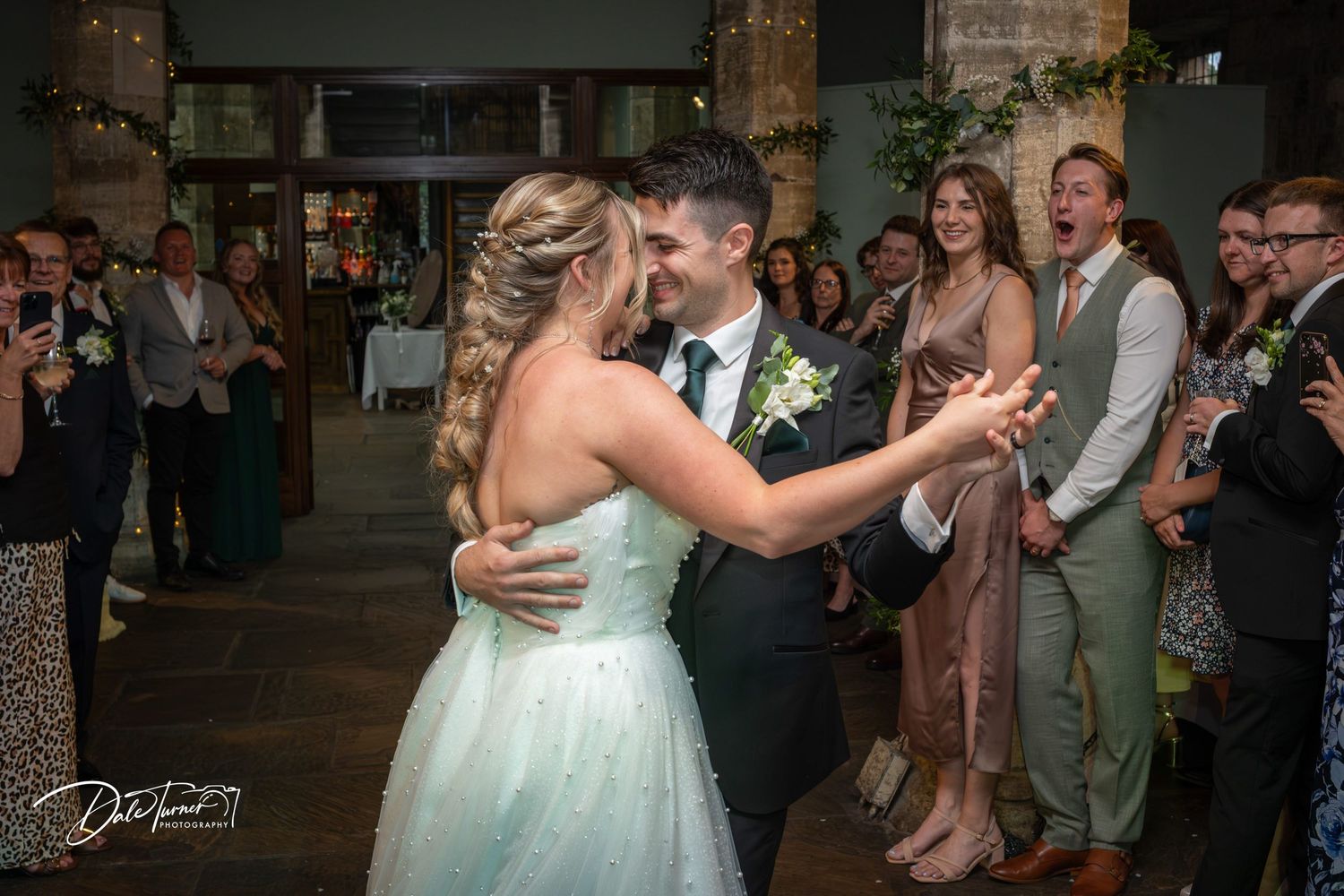 A couple shares their first dance at their wedding reception while guests look on in a rustic venue.