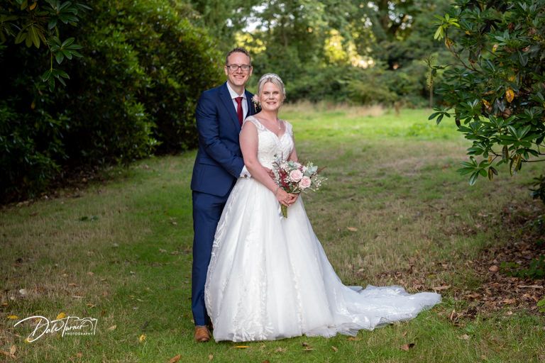 Wedding couple poses together on the grounds of an elegant estate.