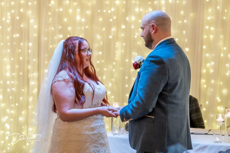 Couple exchanges vows during indoor ceremony with twinkling light backdrop.