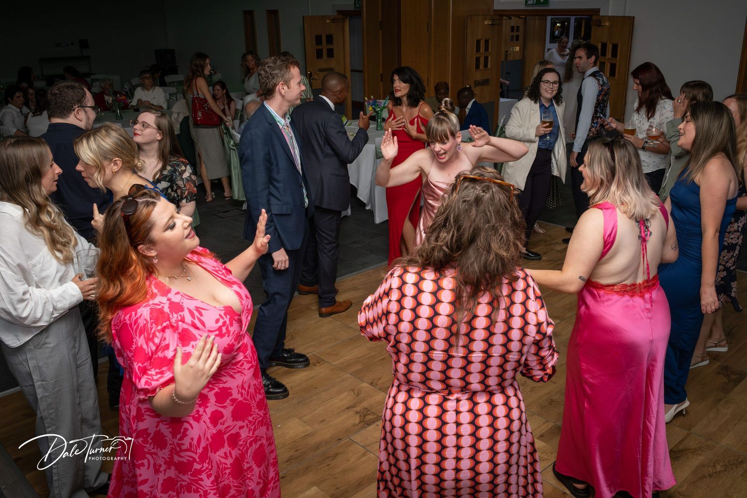 Wedding reception dance party with guests in vibrant pink and red dresses on the dance floor.