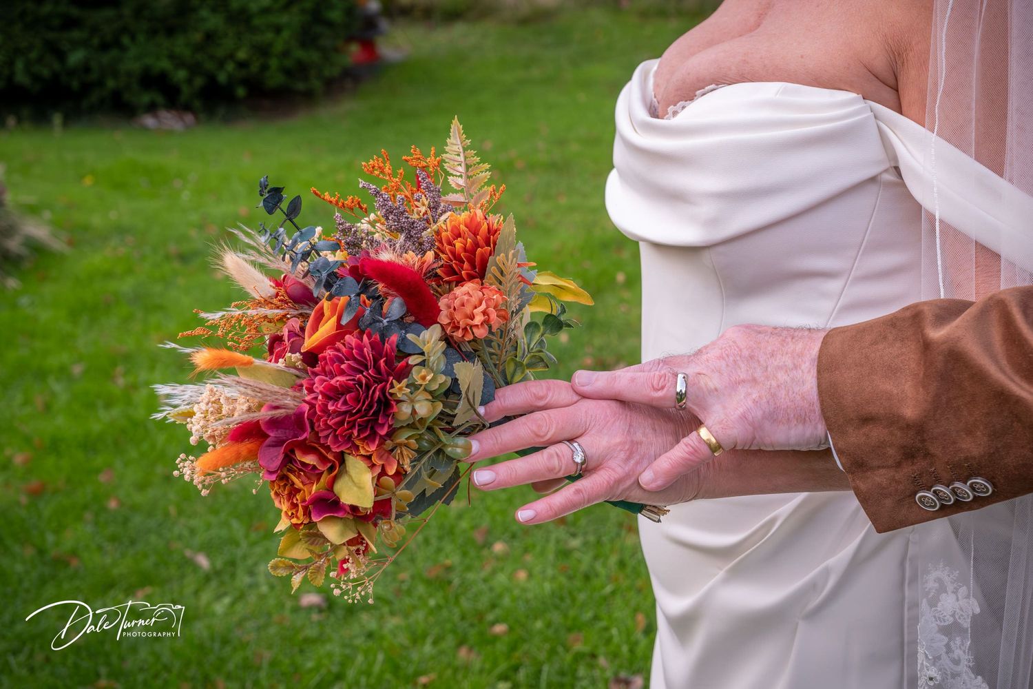 Close-up of vibrant orange and red fall wedding bouquet against white dress.