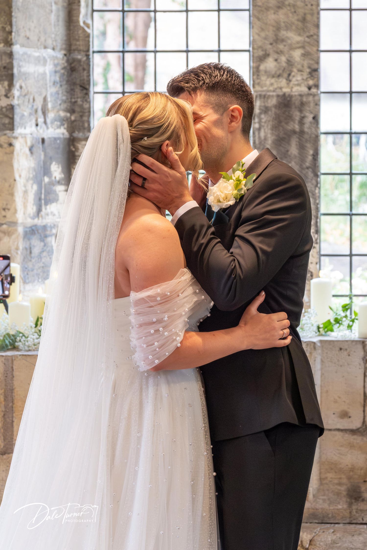 Tender first kiss moment during wedding ceremony in historic stone chapel.