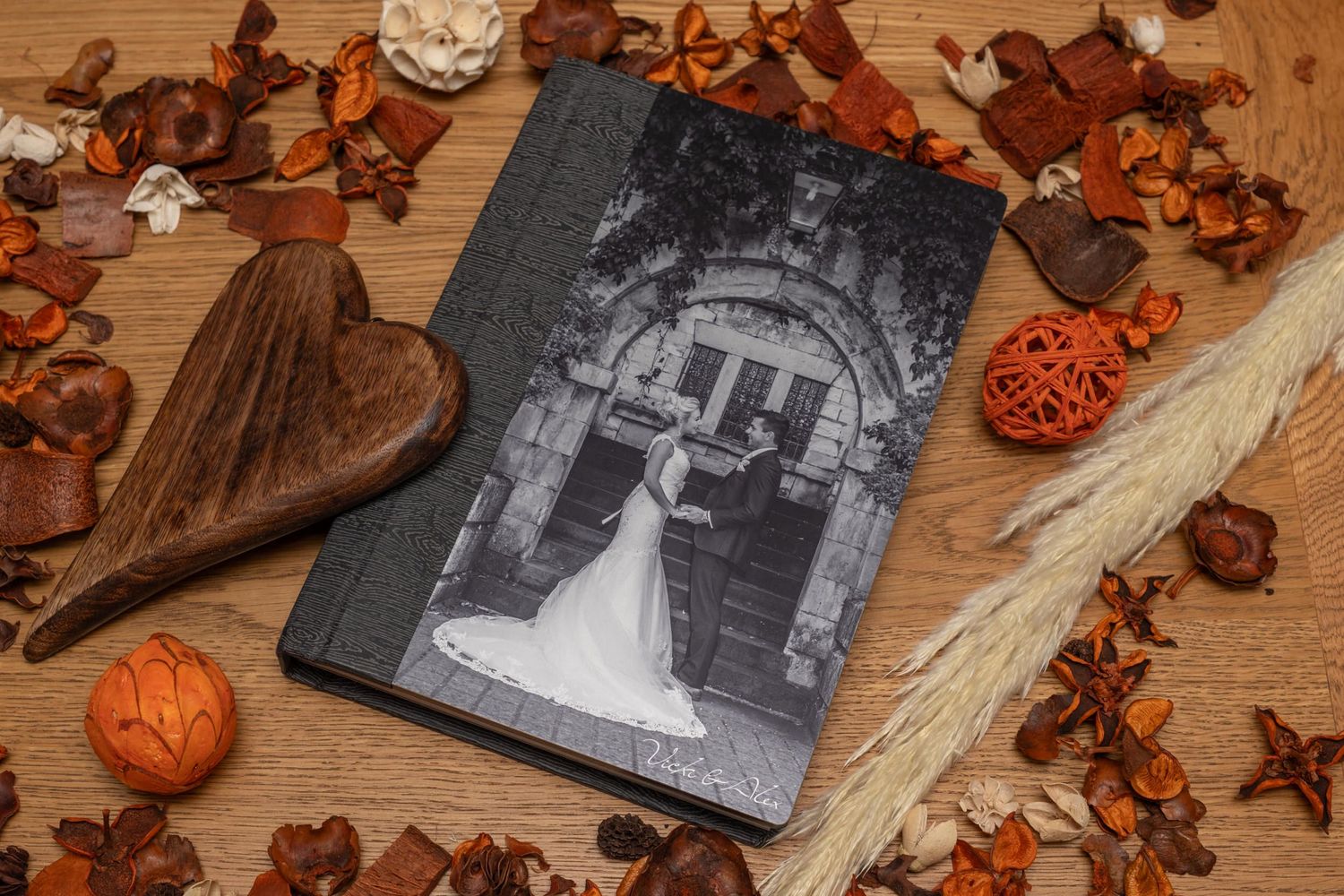 Wedding album displayed on wooden surface with autumn leaves and decorative elements.