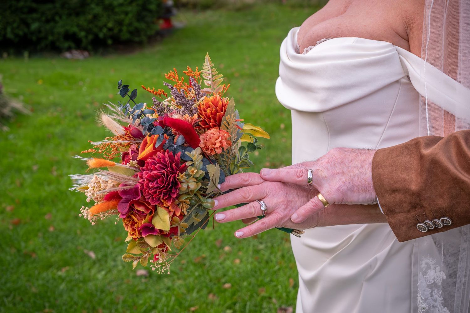 Close-up of hands holding vibrant red and orange autumn wedding bouquet.