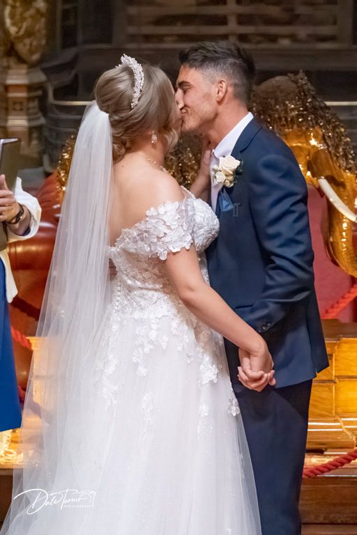 Couple in formal wedding attire standing in luxurious gilded room.