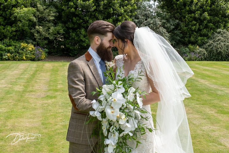 Wedding couple shares an intimate moment outdoors with white floral bouquet.
