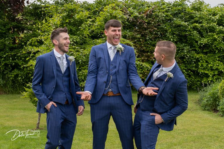 Groomsmen in navy suits share candid moments during outdoor photo session.