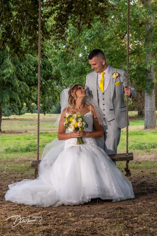 Romantic wedding scene under trees with yellow floral accents and white dress.