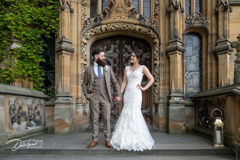 A wedding couple stands beneath an ornate Gothic archway with detailed stone carvings.