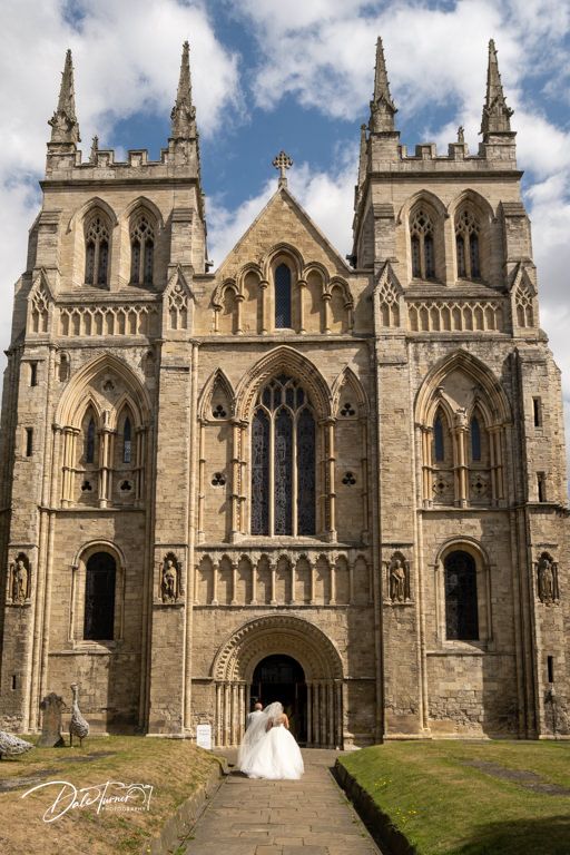 Gothic cathedral exterior with ornate stone architecture and twin spires against blue sky.