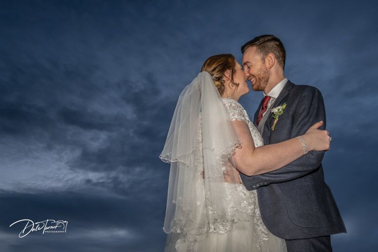 Dramatic wedding portraits against a moody blue sky at sunset show tender moments between newlyweds.