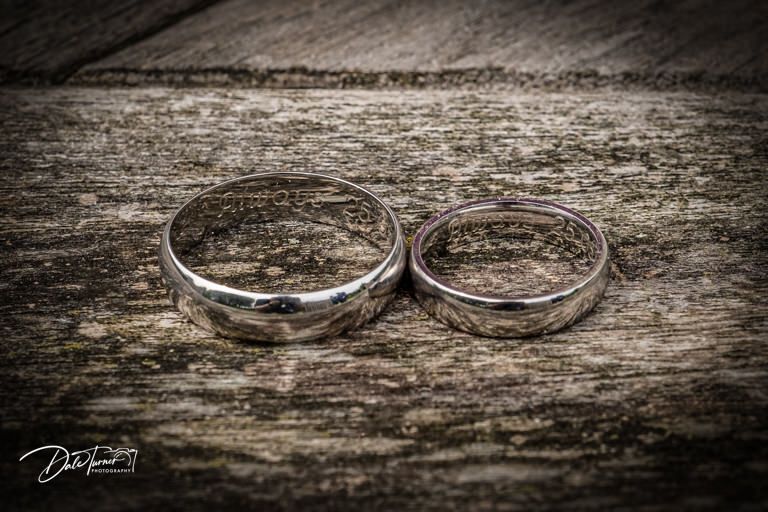 Close-up of wedding rings on weathered wooden surface with dramatic lighting.