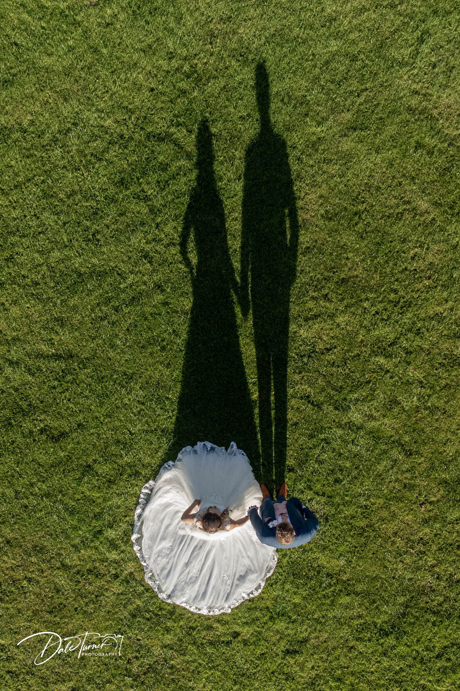 Artistic overhead shot showing couple's shadows cast on green lawn with white wedding dress.