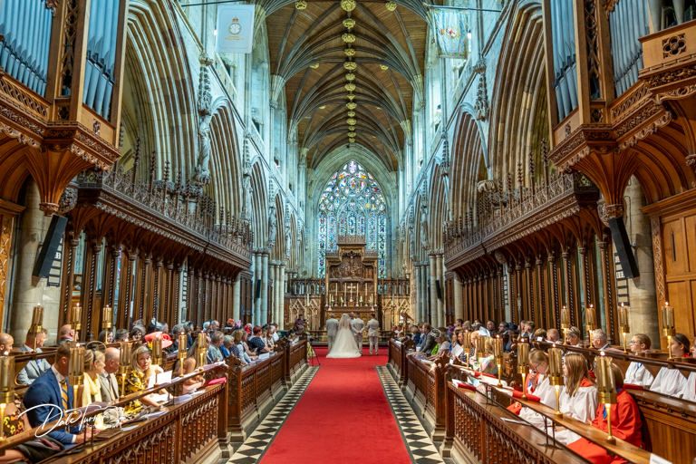 Wide angle view of cathedral's grand nave with guests seated for wedding ceremony.