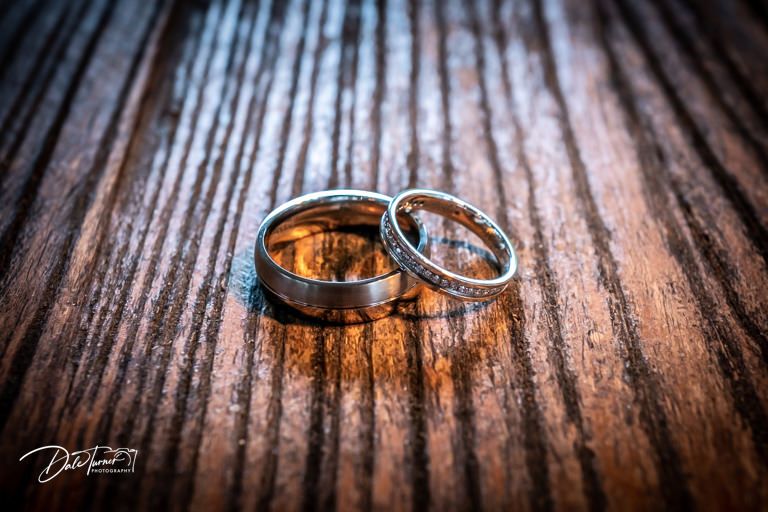 Wedding rings photographed with dramatic lighting on wooden surface.