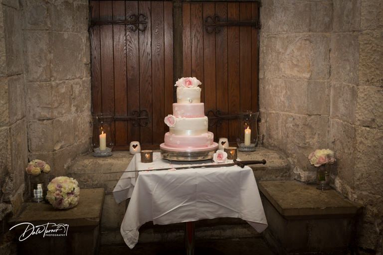 Wedding cake display in rustic stone interior with wooden doors and floral decorations.