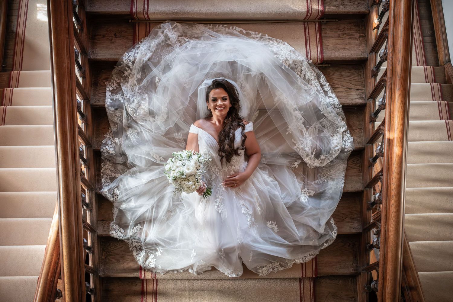 A wedding dress billows out in a perfect circle on wooden stairs creating a stunning overhead view.