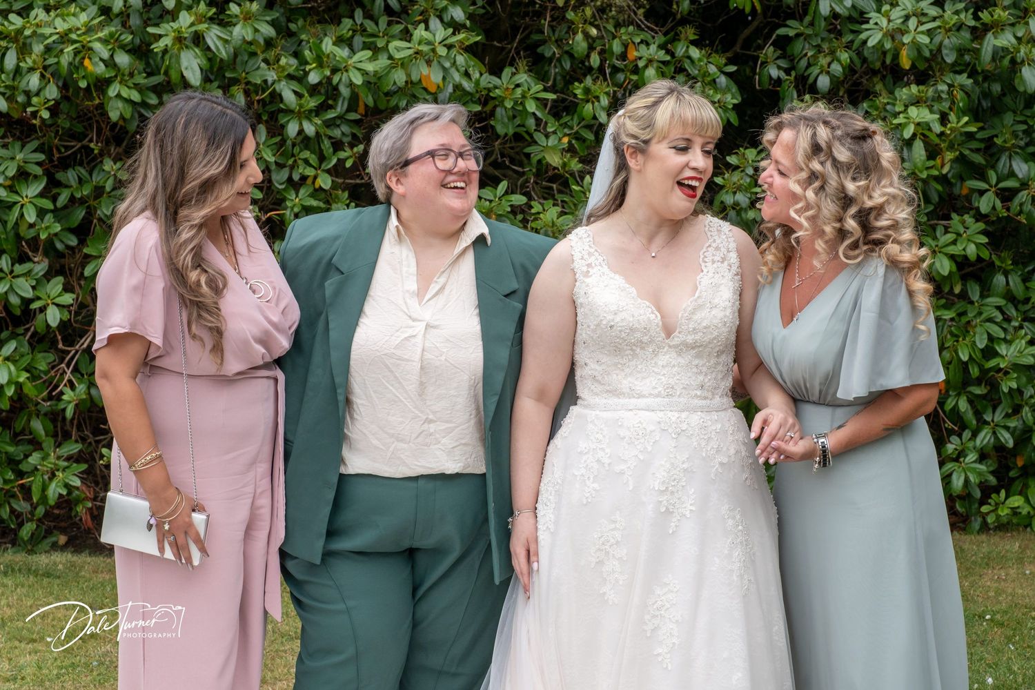 Wedding party members in pastel and white dresses gather for photos in garden setting.