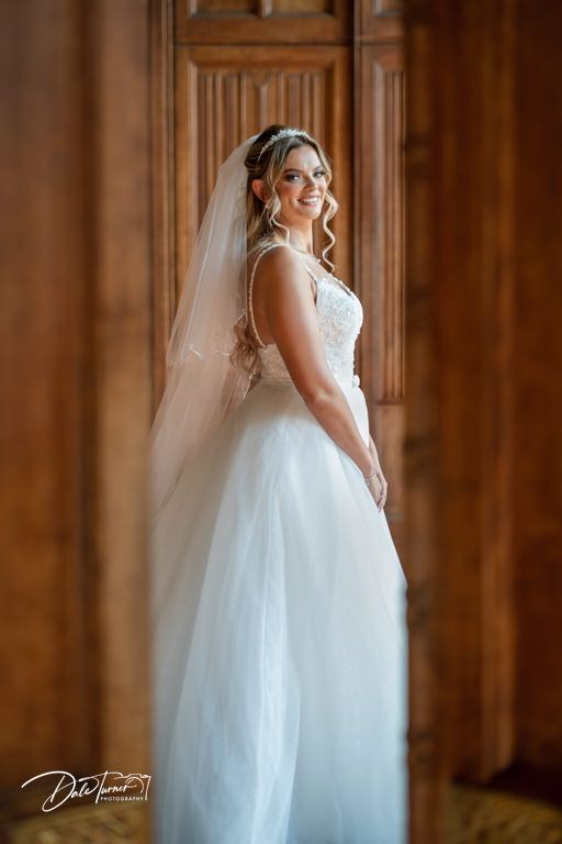 A flowing white wedding gown with delicate details photographed in an elegant wood-paneled room.