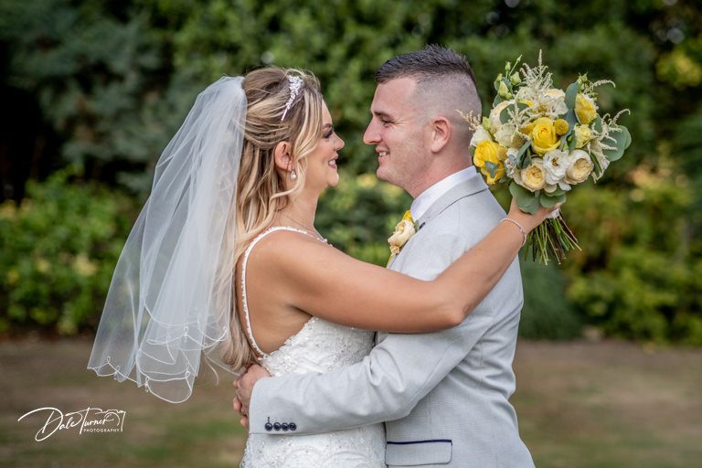 Tender wedding moment photographed in a sunlit garden with yellow floral details.