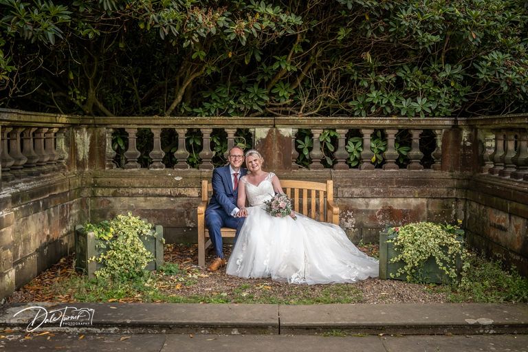 Couple poses for romantic photos on stone balustrade surrounded by greenery.