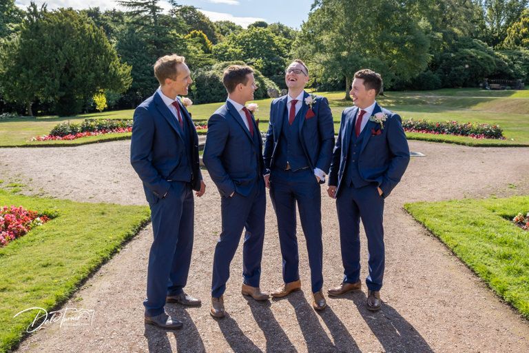 Four groomsmen in matching navy suits standing on a garden path.