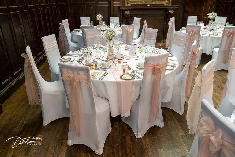 Elegant wedding reception setup with white-covered chairs and tables in a traditional ballroom setting.