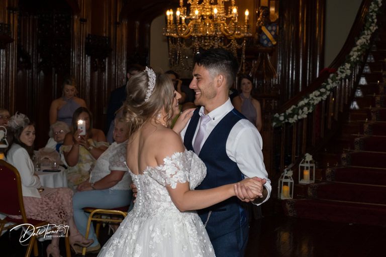 Wedding celebration in an elegant wood-paneled ballroom with chandeliers.