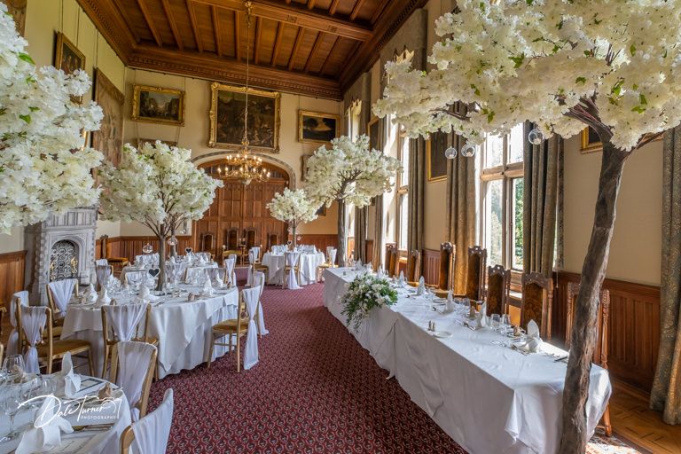 Elegant wedding reception hall with white floral centerpieces and wooden ceiling beams in a historic venue.