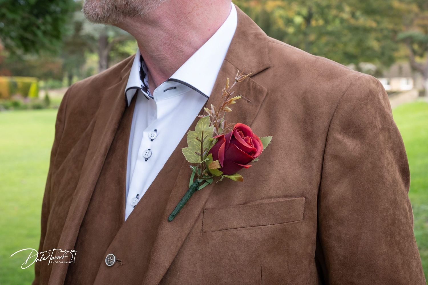 Close-up detail of brown tweed jacket with red rose boutonniere.