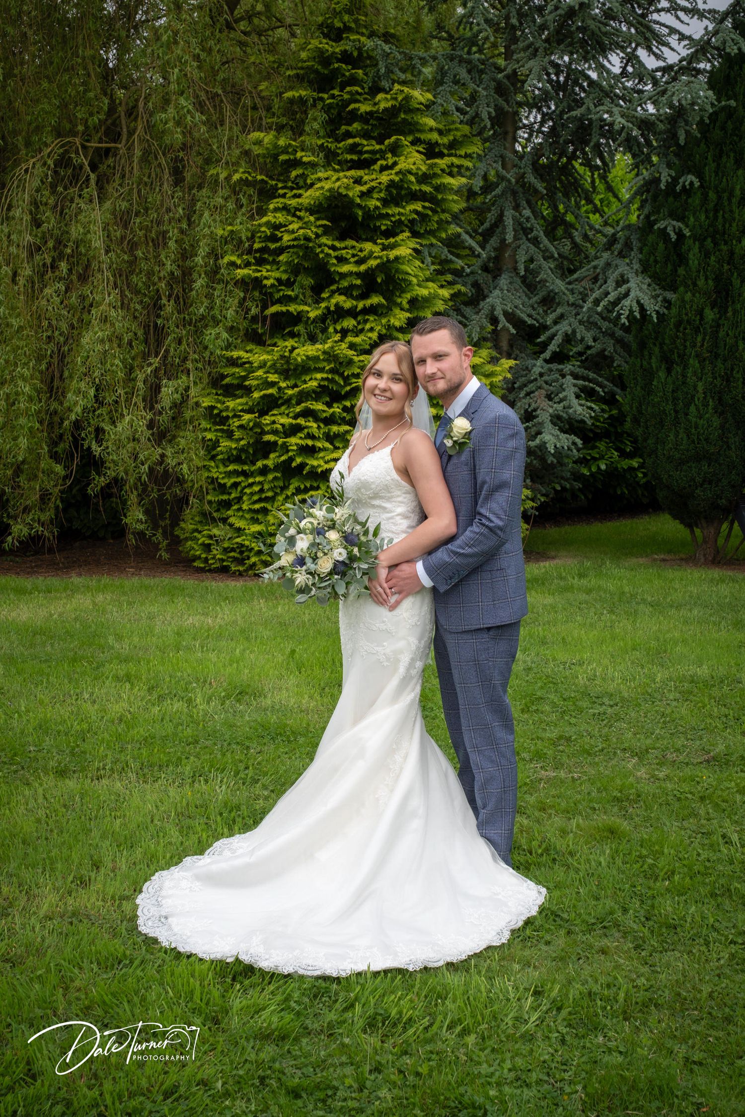 Elegant wedding portraits taken on manicured lawn with evergreen trees in background.