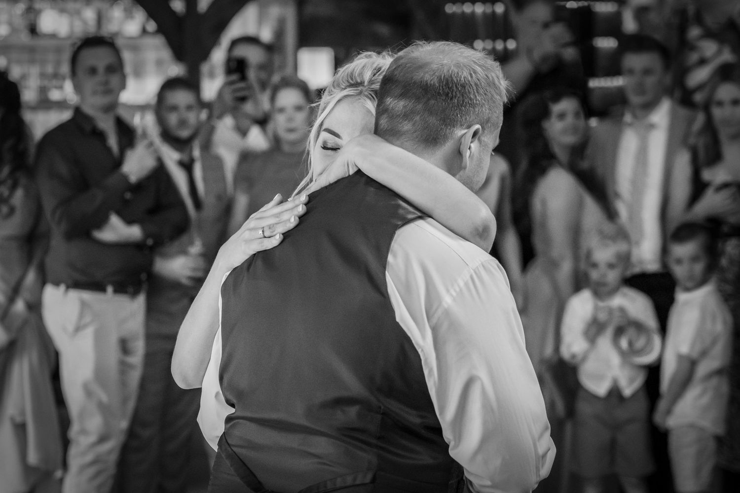 Black and white reception dance photo with crowd of guests in background.