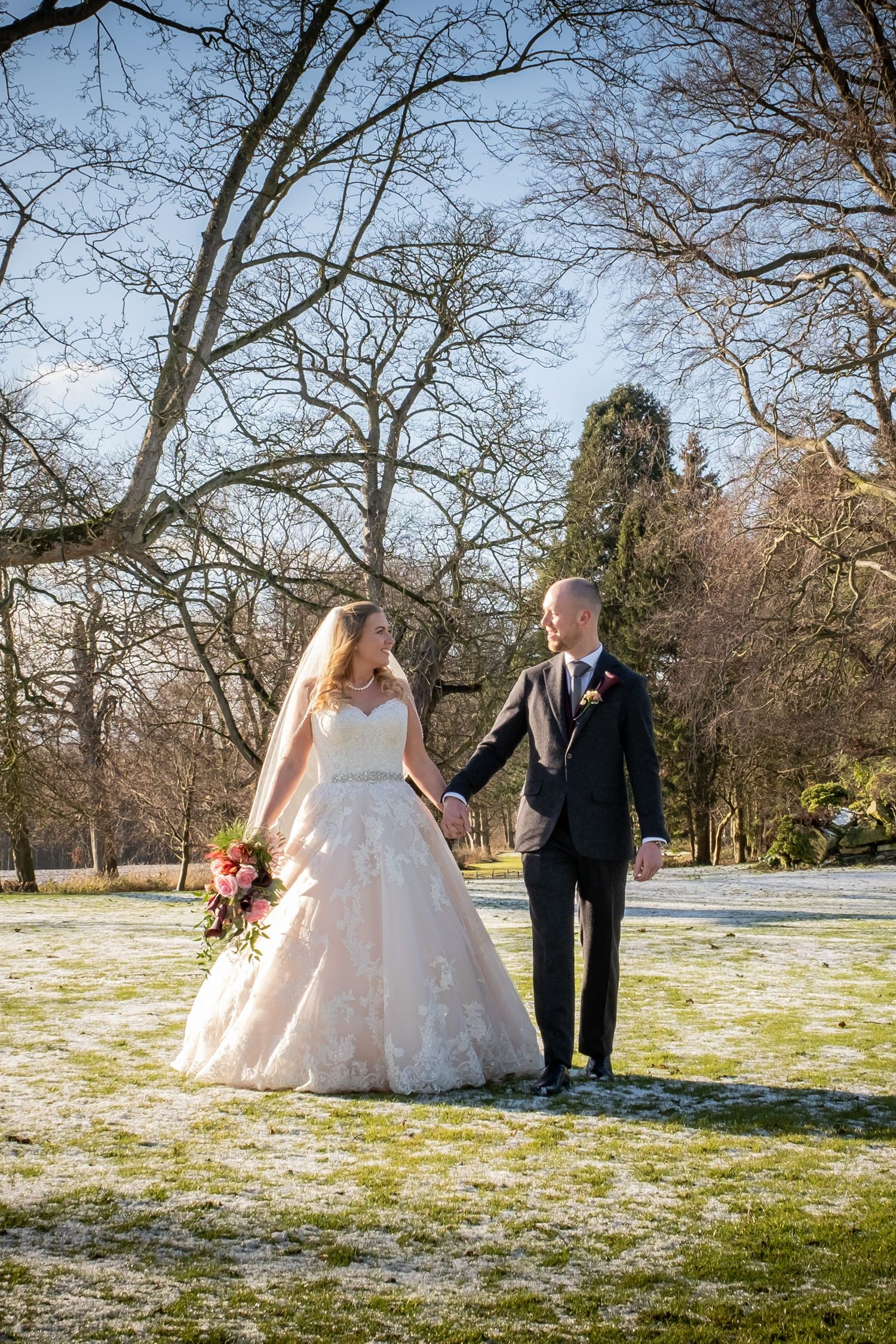 Winter wedding scene with couple walking on snowy ground surrounded by bare trees.