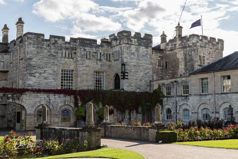 Historic stone castle exterior with manicured gardens and cloudy sky.