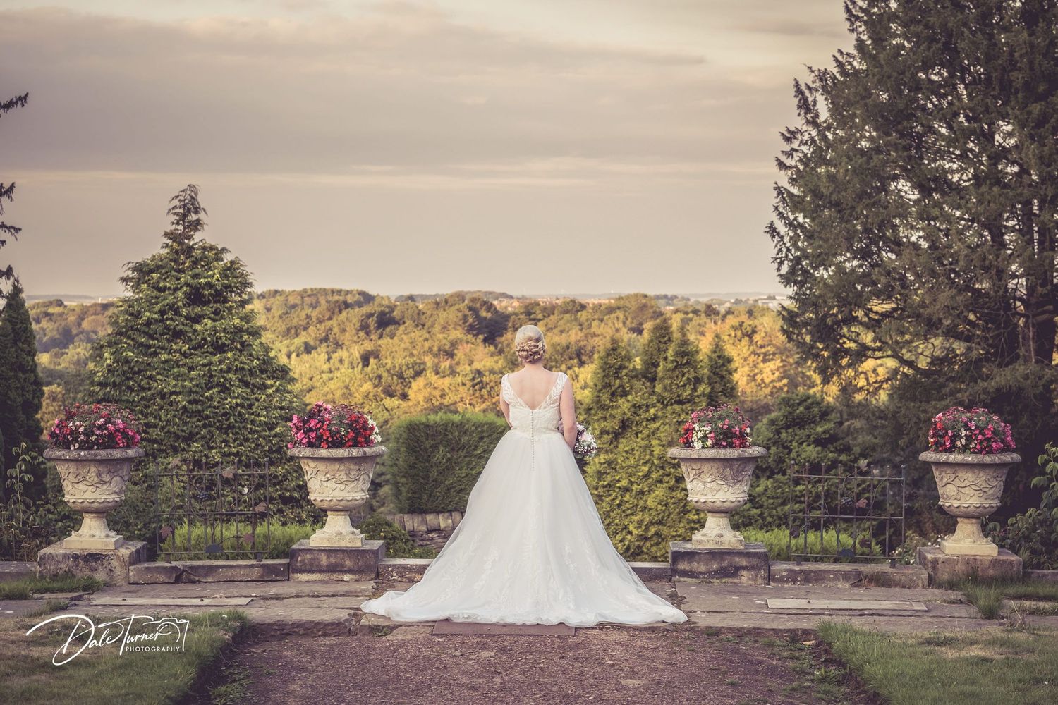 Panoramic wedding photo shoot in an elegant garden setting with decorative stone urns.