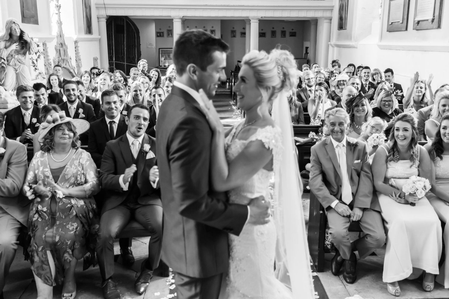 Black and white wedding ceremony photo with guests applauding in background.