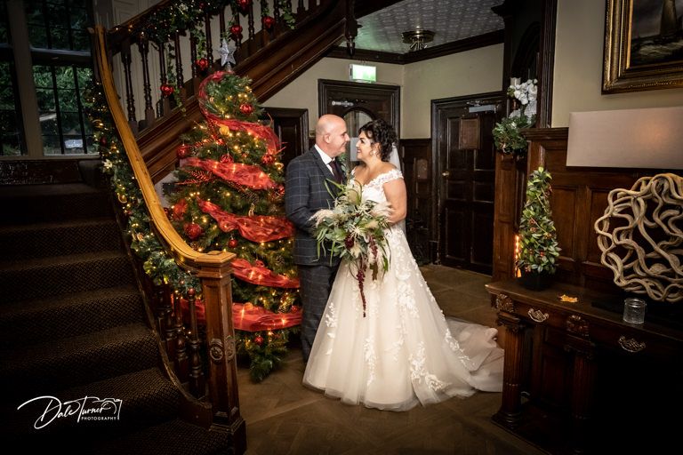 Festive wedding portrait by decorated Christmas staircase with red lights and ornaments.