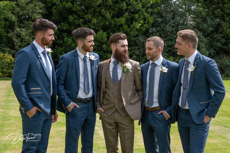 Wedding party in navy suits and one brown suit pose casually outdoors.