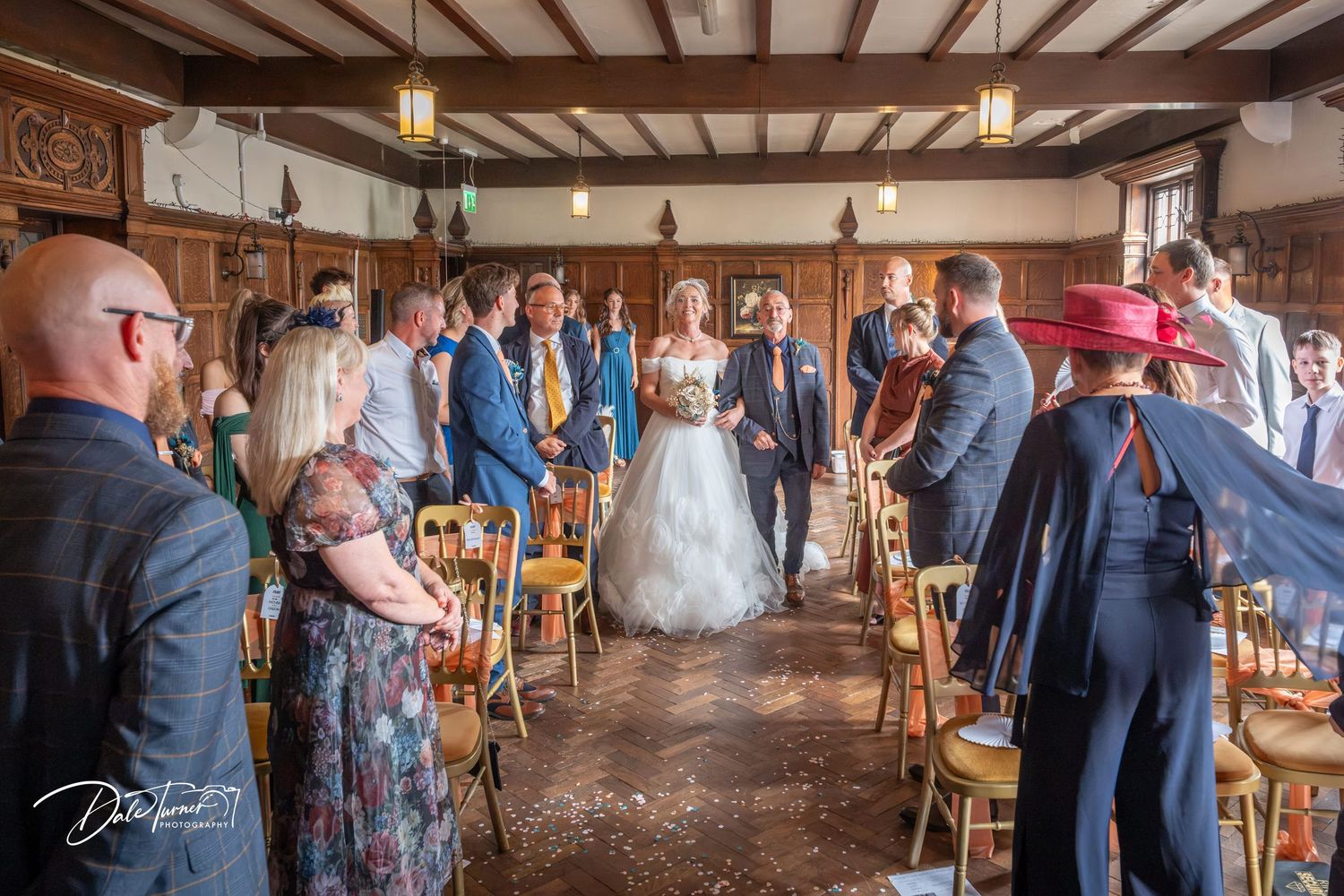 Bride and groom walk down the aisle at a rustic indoor wedding ceremony surrounded by smiling guests.