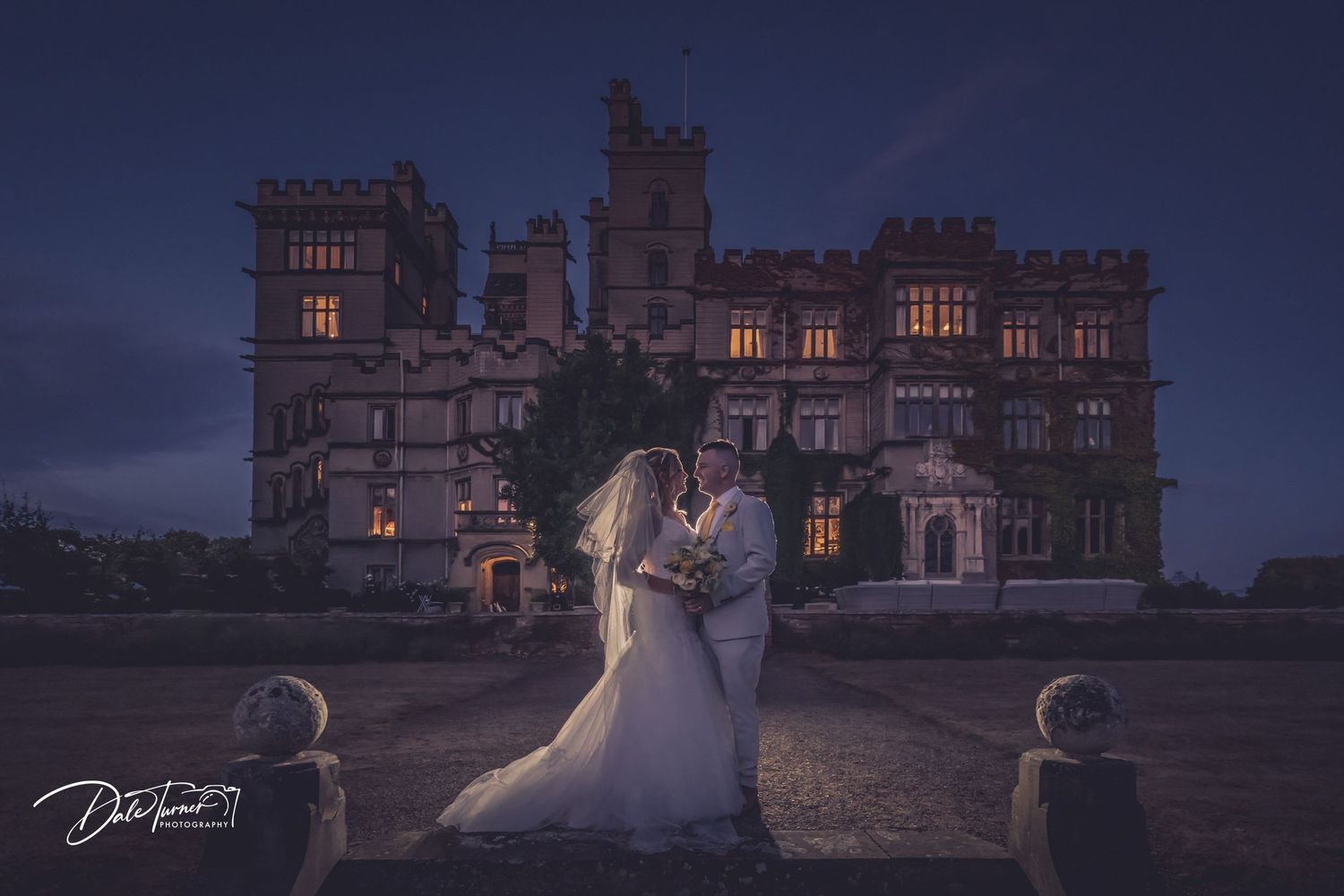 A romantic nighttime wedding photo shoot at an illuminated castle.