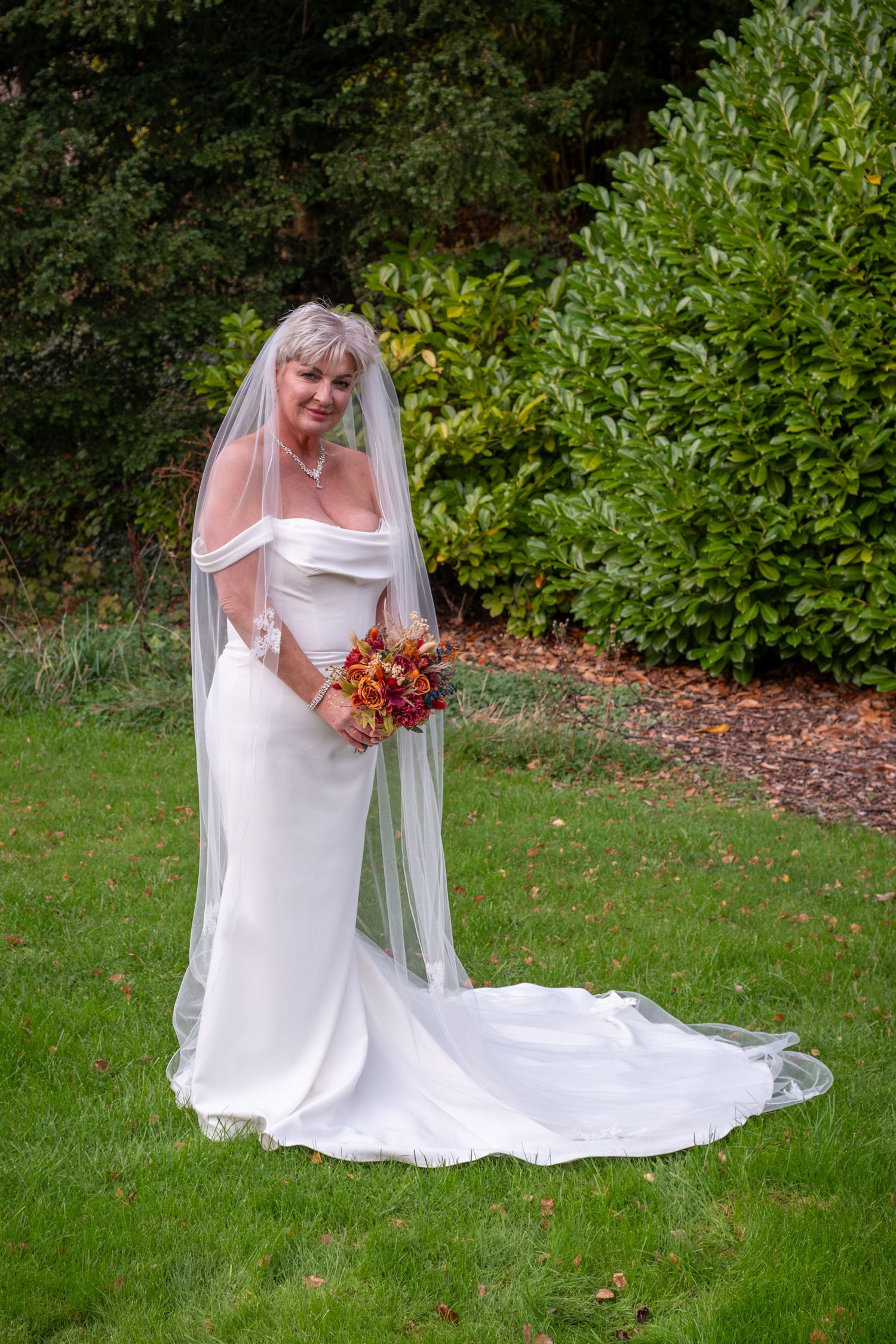 Wedding dress with long train displayed on green lawn with autumn foliage in background.