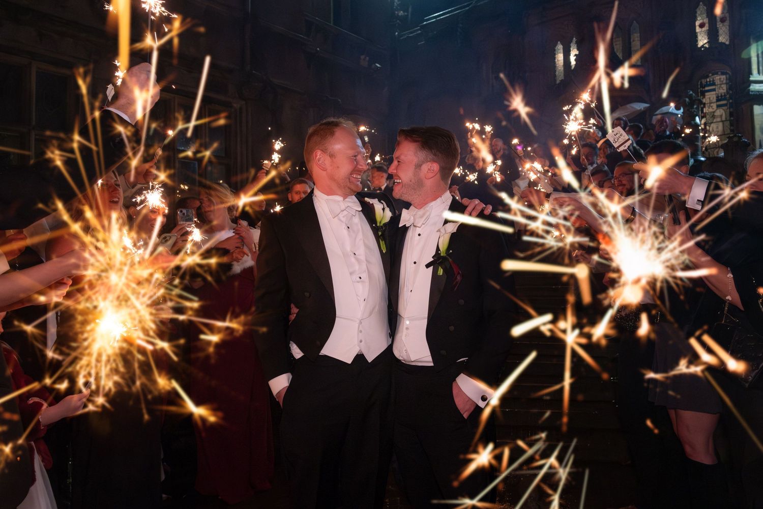 Wedding celebration with sparklers creating magical light trails against dark night sky.