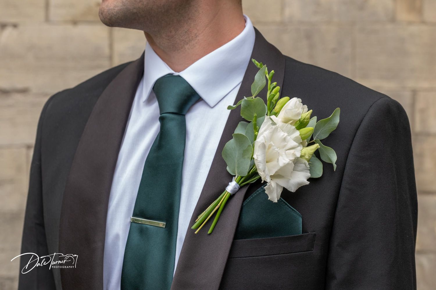 Detail shot of groom's attire showing green tie and white floral boutonniere.