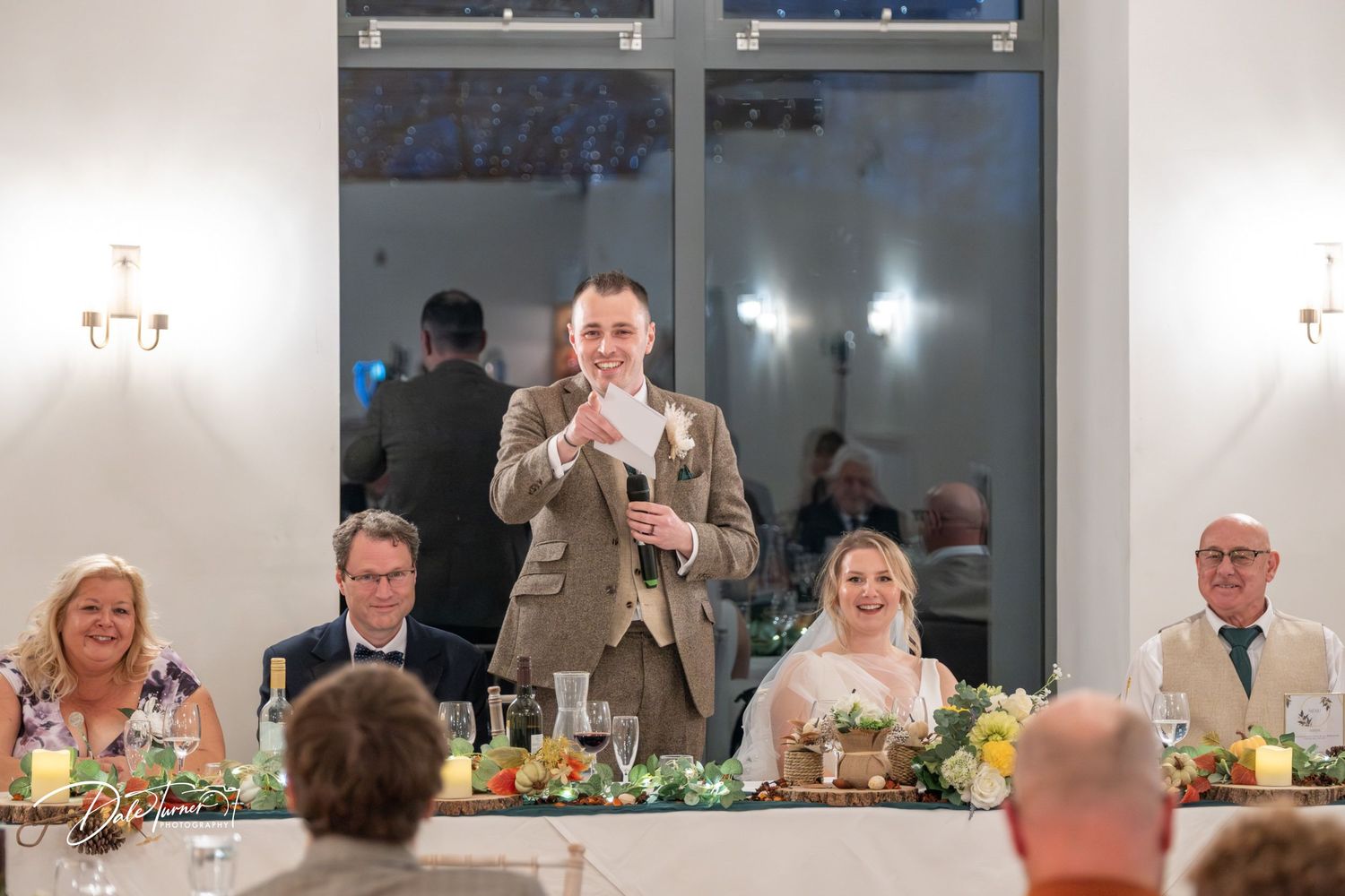 Wedding reception guests seated at long tables decorated with floral centerpieces and glassware.