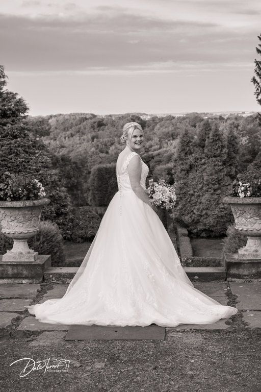 Dramatic black and white wedding portraits showcase flowing dress against hillside landscape.